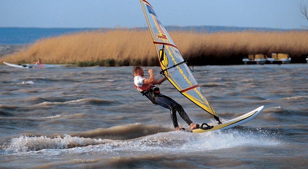 Ein Mann windsurft auf einer welligen See, hält mit einer Hand das Segel fest und balanciert auf einem Board.