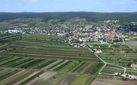 Luftaufnahme einer ländlichen Stadt, umgeben von üppigen grünen Feldern, Hügeln in der Ferne und einem klaren blauen Himmel.