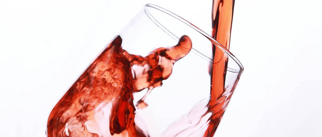 Eine Nahaufnahme von rotem Wein, der in ein klares Weinglas gegossen wird, wobei etwas auf die Seiten spritzt.