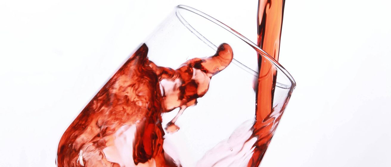 Eine Nahaufnahme von rotem Wein, der in ein klares Weinglas gegossen wird, wobei etwas auf die Seiten spritzt.