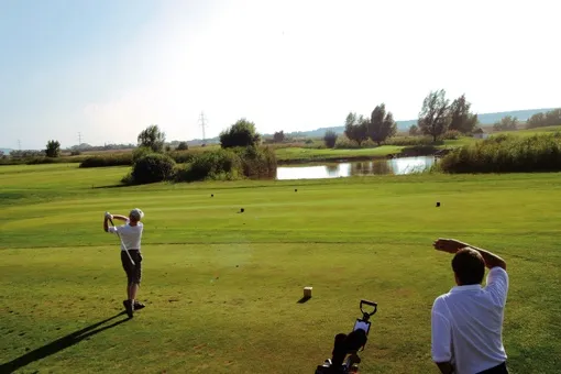 Zwei Männer spielen Golf auf einem Golfplatz. Ein Mann schwingt den Golfschläger.
