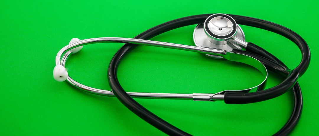 Ein Stethoskop liegt auf einem grünen Hintergrund. Es hat einen schwarzen Gummischlauch und ein silbernes Bruststück.