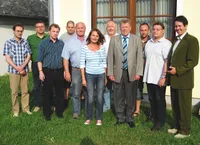 Eine Gruppe von Menschen, darunter Männer und Frauen, steht auf einem Rasen vor einem Gebäude und posiert möglicherweise für ein Foto.
