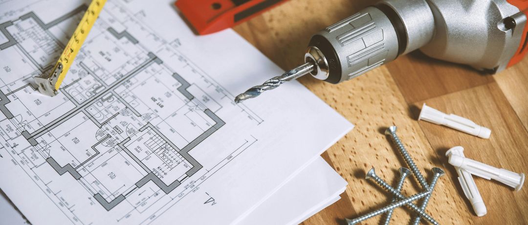 Eine Flachdarstellung eines Holztisches mit einer Bohrmaschine, einem Maßband, einem Wasserwaage und Schrauben darauf. Ein Stück Papier mit einem Grundriss liegt auf dem Tisch.