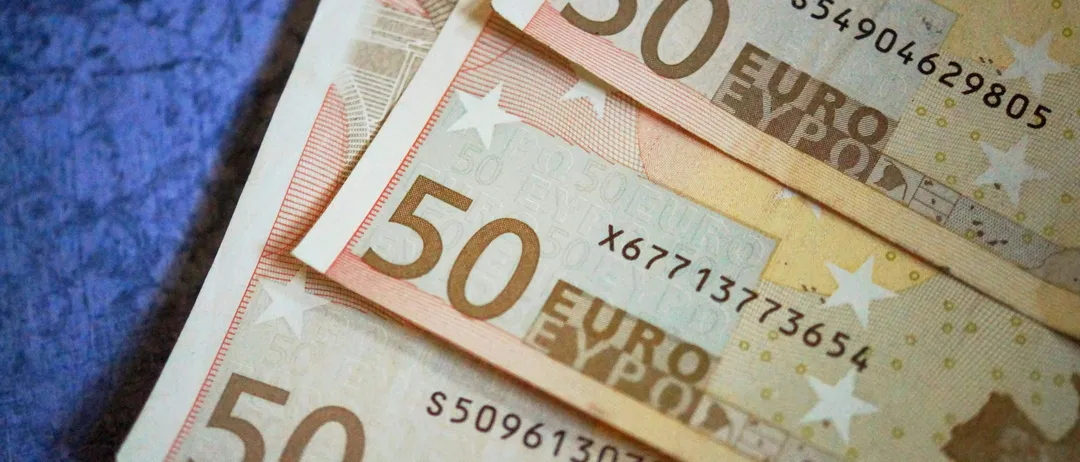 Ein Stapel von fünf 50-Euro-Scheinen ist zu sehen, jeder mit unterschiedlichen Seriennummern. Die Scheine sind auf einer Kombination aus Weiß, Rosa und Braun gedruckt.