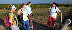 Fünf Erwachsene stehen in einem Feld, möglicherweise auf einer Tour, tragen verschiedene Kleidungsstücke und Accessoires. Sie schauen in verschiedene Richtungen.