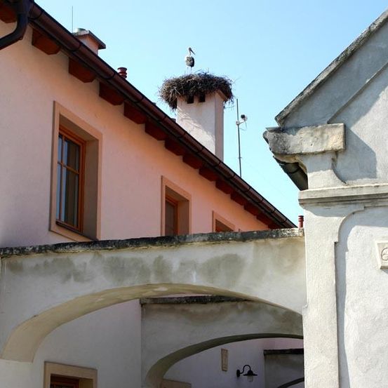 Ein Gebäude mit einem Vogelnest auf dem Dach, einem Schornstein und einer Lampe unter einem Torbogen.