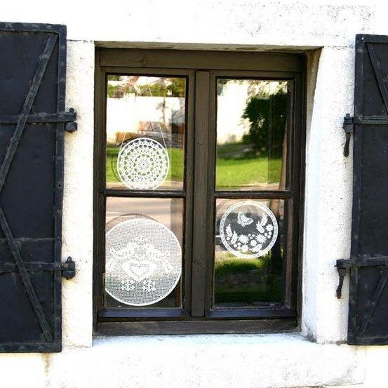 Eine weiße Wand mit einem geschlossenen Fenster. Das Fenster hat zwei dekorative Spitzenvorhänge, die daran hängen. Die Vorhänge haben ein Herz- und Schmetterlingsdesign.