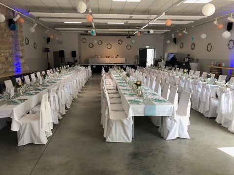 Ein großer Bankettsaal mit langen Tischen und Stühlen, die mit weißen Tüchern bedeckt und mit Blumen und Ballons dekoriert sind, für eine Veranstaltung vorbereitet.