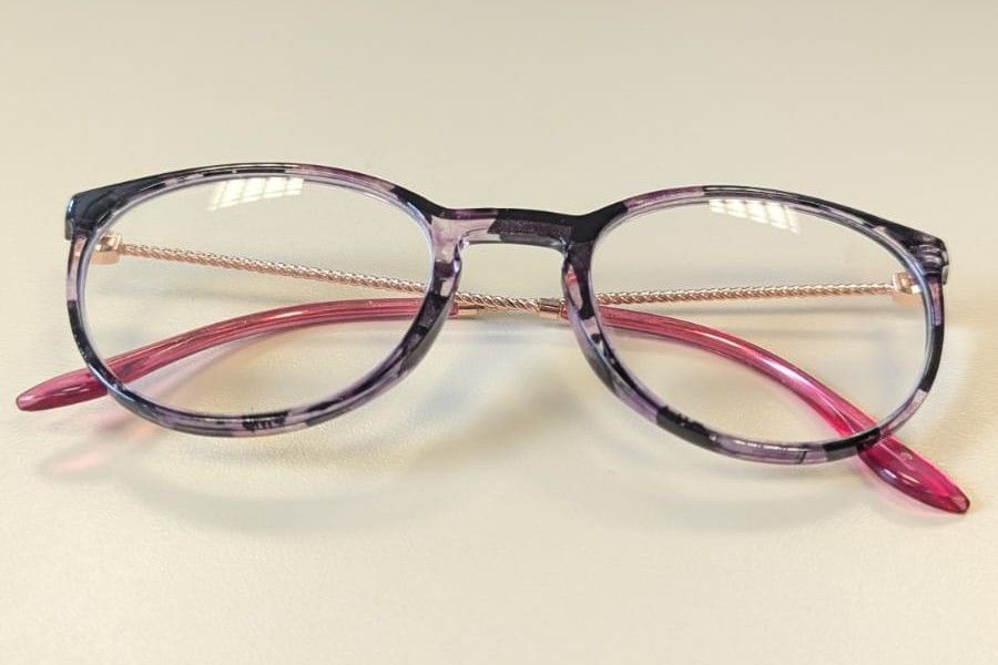Ein Brillenpaar mit klaren Gläsern und lila Rahmen. Die Gläser haben einen Farbverlauf von klar zu lila.