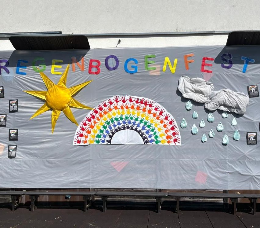 Ein farbenfrohes Banner mit dem Schriftzug 'Egenbogenfest' in verschiedenen Farben. Es zeigt einen großen Regenbogen, eine Sonne und einige Regentropfen. Das Banner ist wahrscheinlich für eine Veranstaltung.