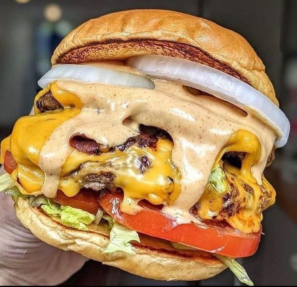 Ein Nahaufnahme eines Hamburgers mit Speck, geschmolzenem Käse, Tomate und Zwiebeln auf einem getoasteten Brötchen.