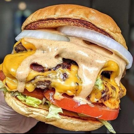 Ein Nahaufnahme eines Hamburgers mit Speck, geschmolzenem Käse, Tomate und Zwiebeln auf einem getoasteten Brötchen.