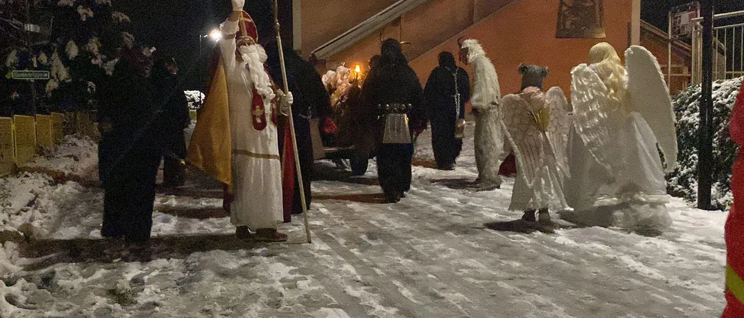 Eine Gruppe von Menschen in Kostümen, darunter eine Person als Weihnachtsmann verkleidet, steht nachts im Schnee.