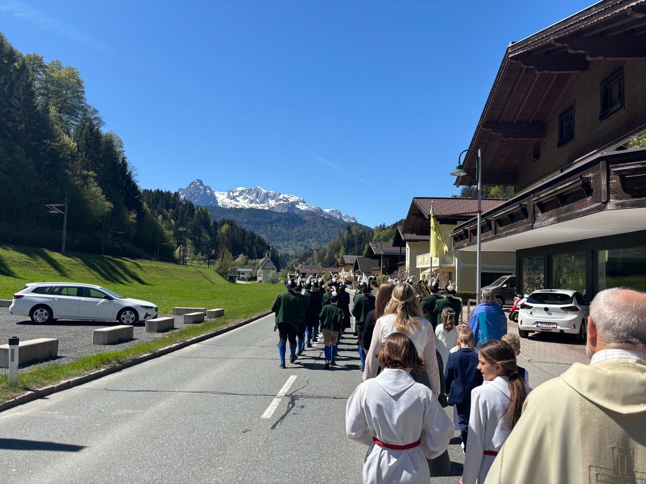 Ein Umzug in traditioneller Kleidung, der auf einer Straße mit Bergen und Häusern im Hintergrund läuft.