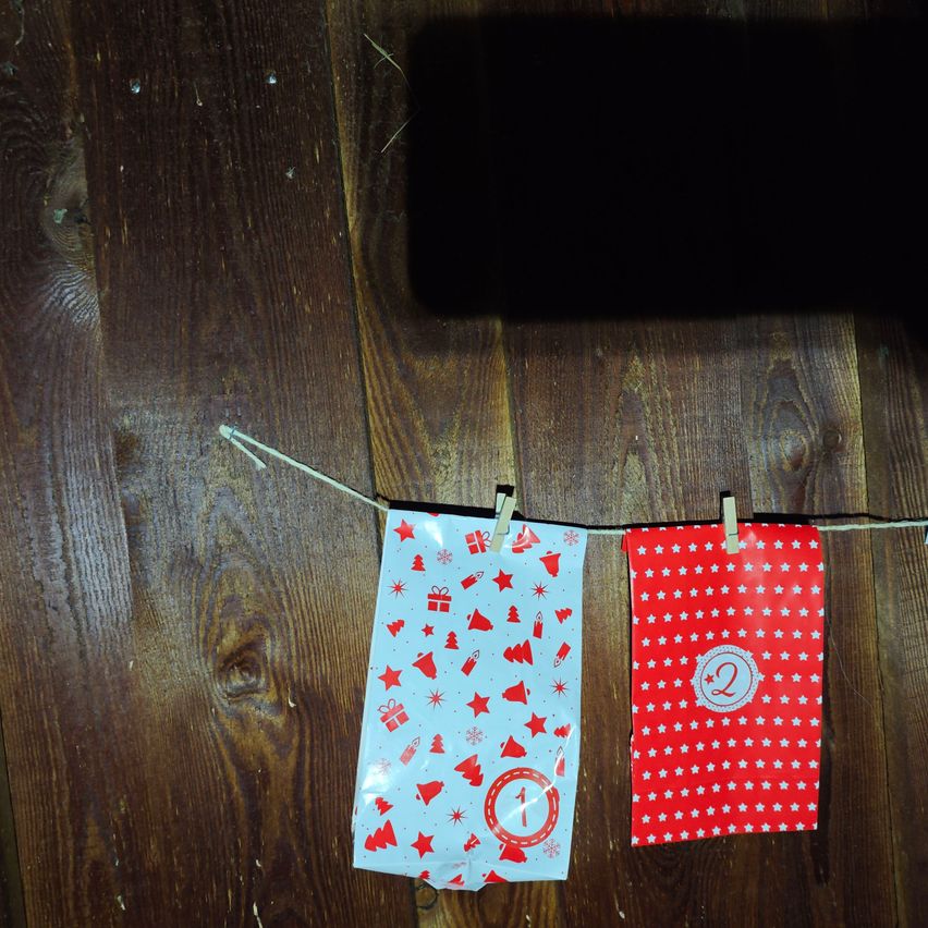 Zwei festliche rote und weiße Tüten mit Sternen und den Zahlen 1 und 2 hängen an einer Schnur auf einem hölzernen Hintergrund.
