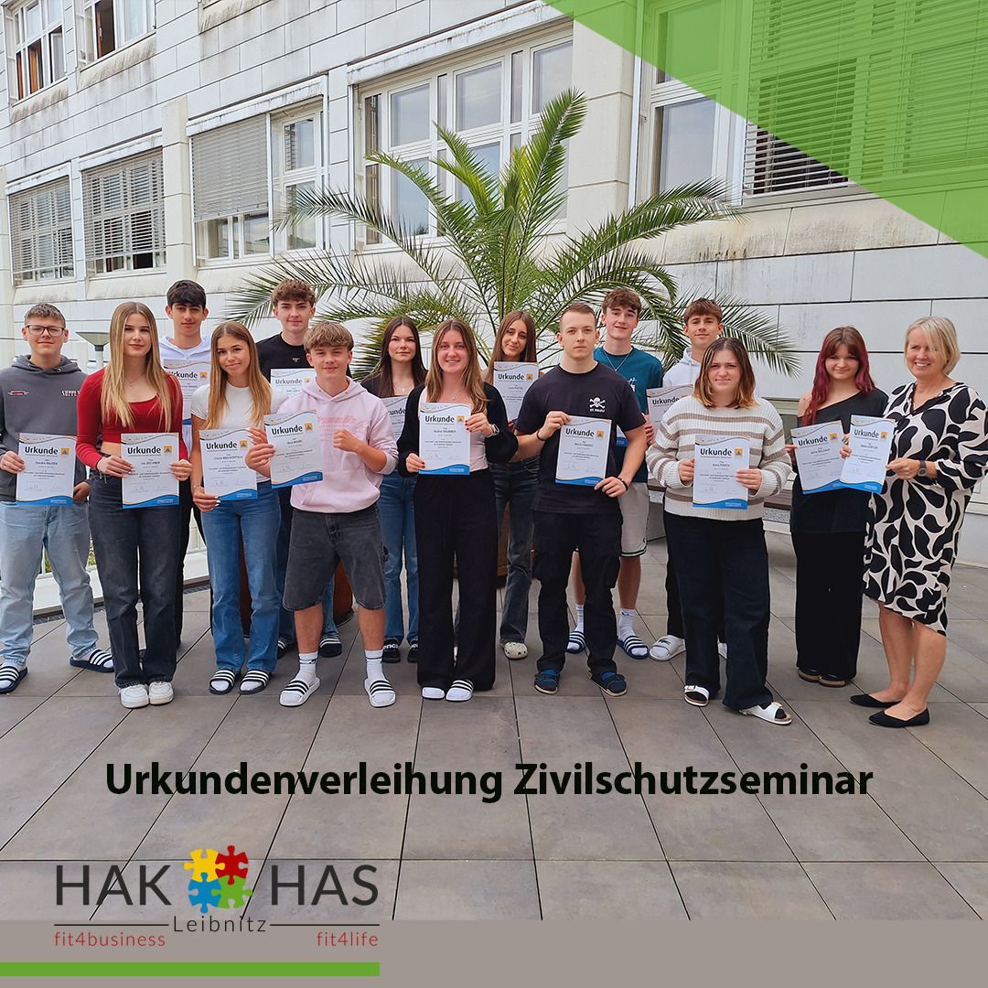 Eine Gruppe von Schülern posiert mit Urkunden vor einem Gebäude, mit einer Palme in der Mitte und einem Schild, das Urkundenverleihung Zivilschutzseminar steht.