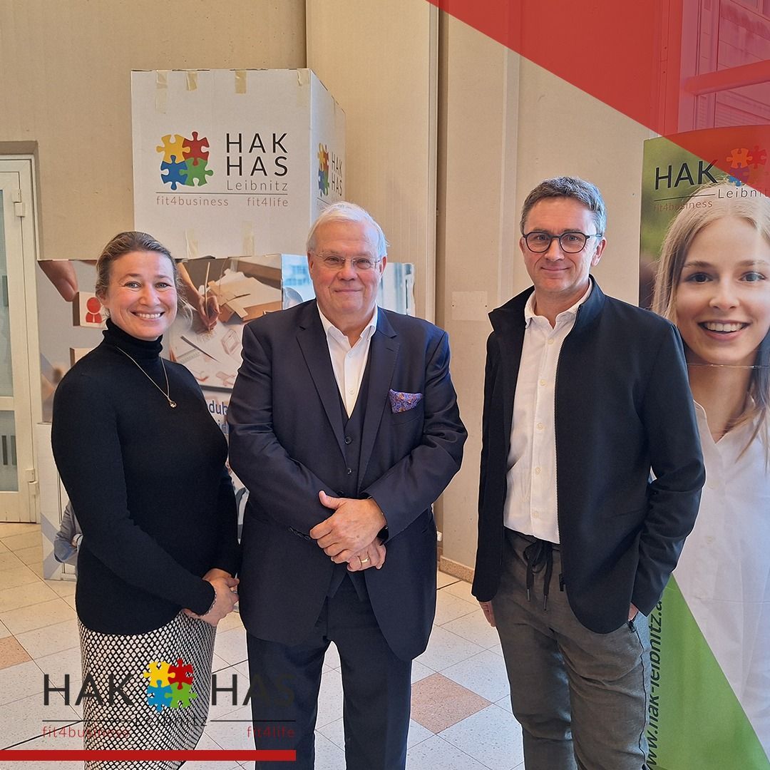 Drei Personen stehen gemeinsam vor einem Hintergrund mit Hak Has Branding. Der Mann in der Mitte trägt einen Anzug, die anderen tragen Geschäftskleidung. Alle lächeln.