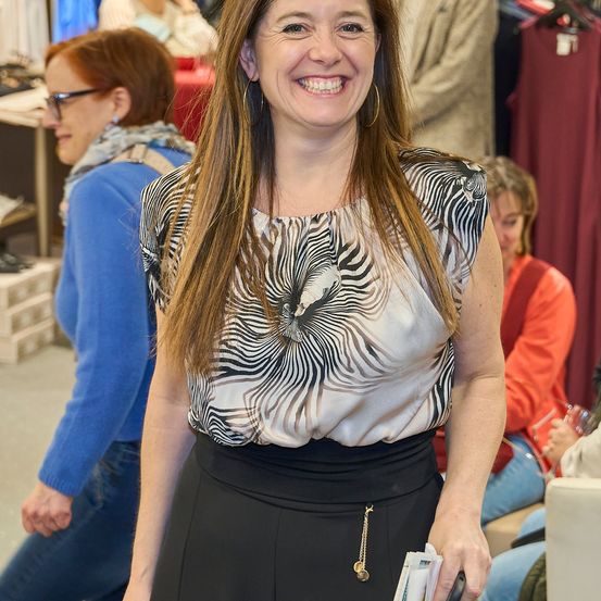 Eine Frau mit langen Haaren, die ein Zebra-Print-Oberteil und schwarze Hose trägt, lächelt in einem Bekleidungsgeschäft.