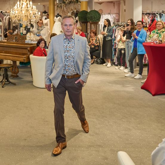 Ein Mann in einem Anzug geht durch einen Bekleidungsladen, während die Leute zusehen und klatschen.