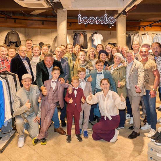 Eine Gruppe von Menschen in formeller Kleidung posiert für ein Foto in einem Bekleidungsgeschäft mit einem ikonischen Schild.