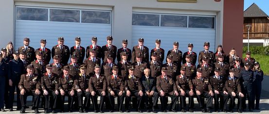 A group of firefighters in uniform pose for a photo in front of the W. Feuerwehr Schamberg building.