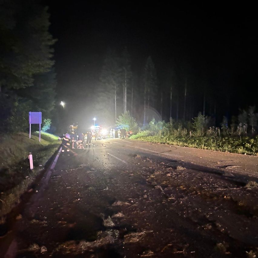 Rettungskräfte sind am Unfallort einer nächtlichen Unfallstelle auf einer Landstraße, mit verstreutem Schutt und mehreren versammelten Personen in der Nähe.