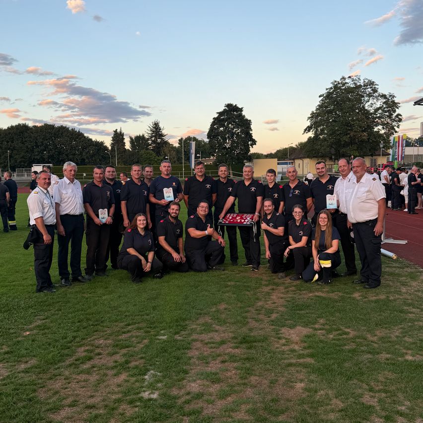 A group of firefighters in uniform pose for a photo on a field with a sunset in the background.