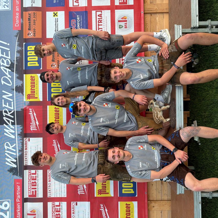 Eine Gruppe von Personen in grauen T-Shirts, Shorts und Sneakers posiert für ein Foto. Sie lächeln und stehen vor einem roten und weißen Hintergrund. Sie scheinen Teil eines Teams zu sein.