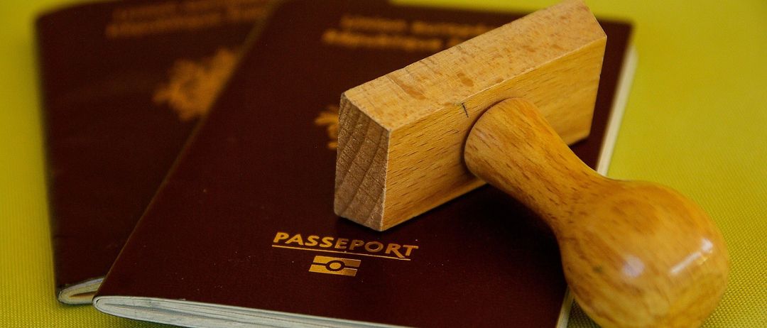 Ein Passbuch mit einem hölzernen Stempel liegt auf einer gelben Oberfläche. Ein weiteres Passbuch ist teilweise dahinter sichtbar.