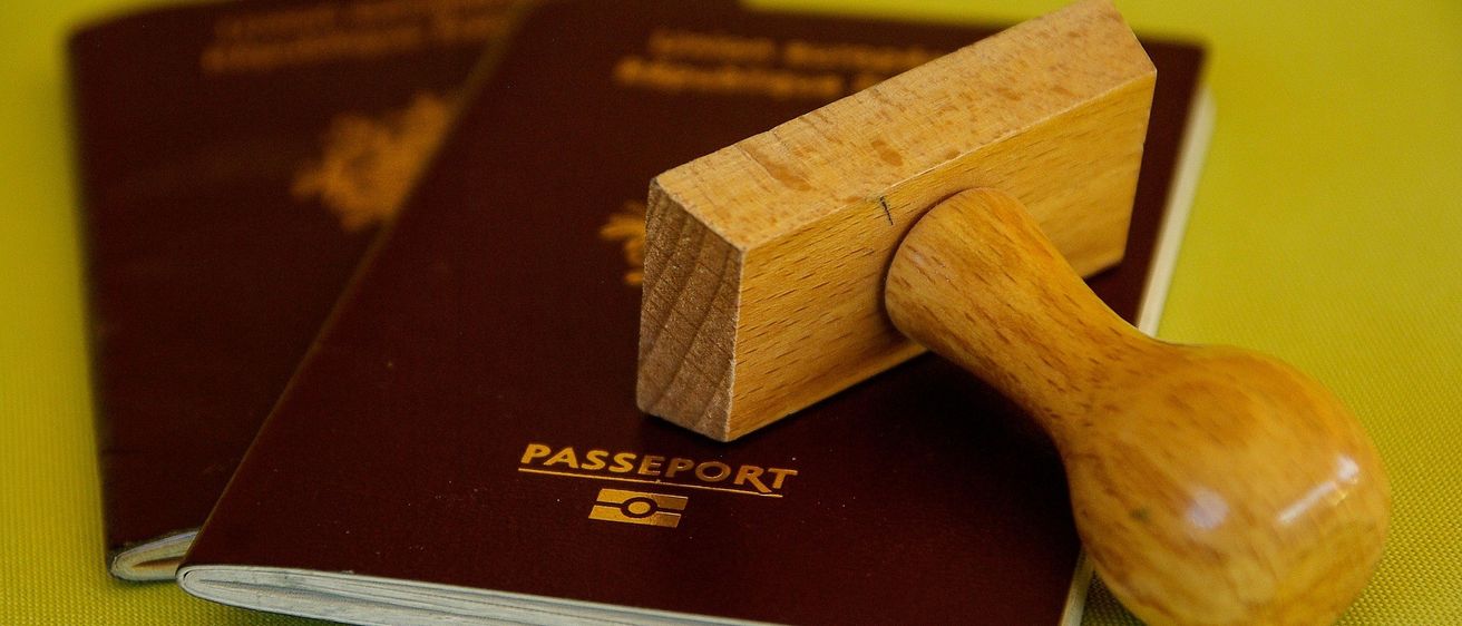 Ein Passbuch mit einem hölzernen Stempel liegt auf einer gelben Oberfläche. Ein weiteres Passbuch ist teilweise dahinter sichtbar.