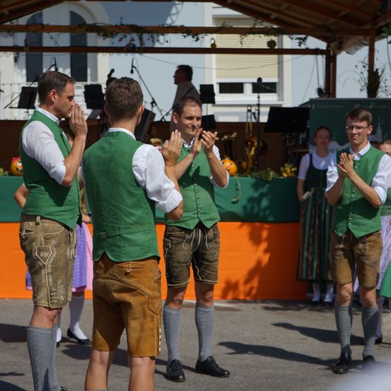 Vier Männer in grünen Westen und braunen Shorts klatschen vor einer Bühne mit Hintergrund und Musikinstrumenten.
