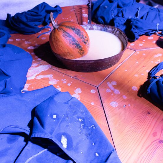Ein Kürbis in einer Schüssel mit Milch, umgeben von blauen Stoffen auf einem Holztisch.