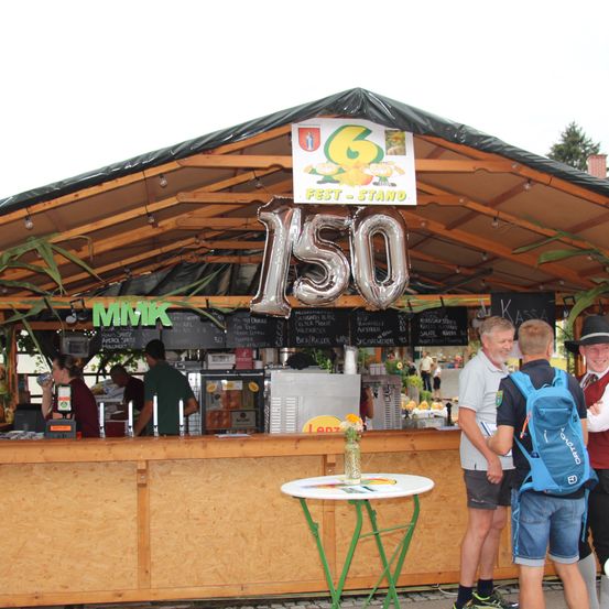 Ein Essensstand mit einer 150-Ballon, einem Schild, das Fest-Stand steht, und Leute, die davor stehen.