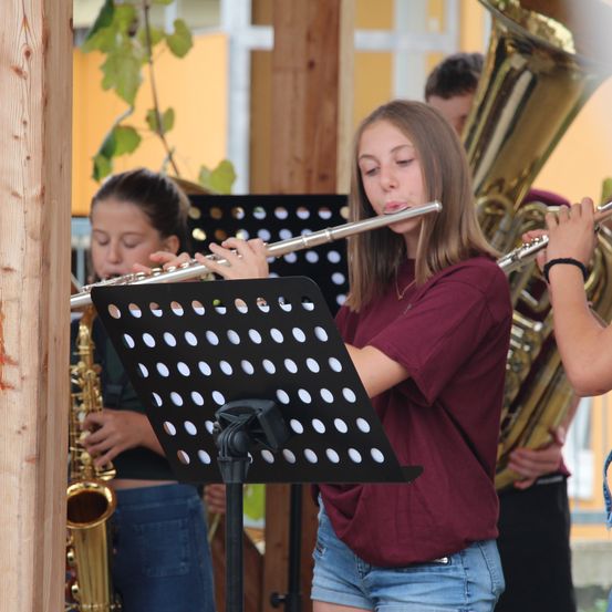 Ein junges Mädchen spielt Flöte in einer Outdoor-Band mit einem Saxophonisten und einem Tubaspieler hinter ihr.