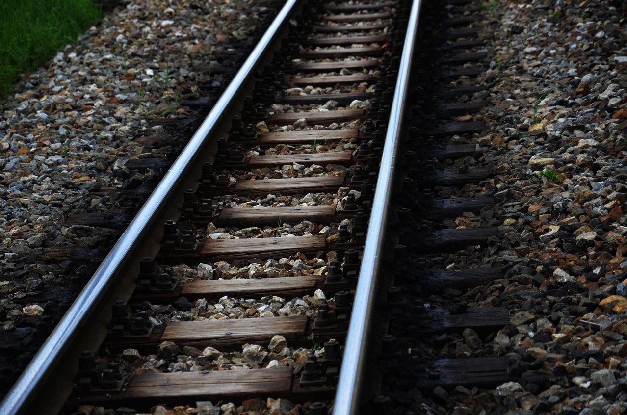 A close-up view of a railway track with gravel and wooden ties, showing the steel rails and fasteners.
