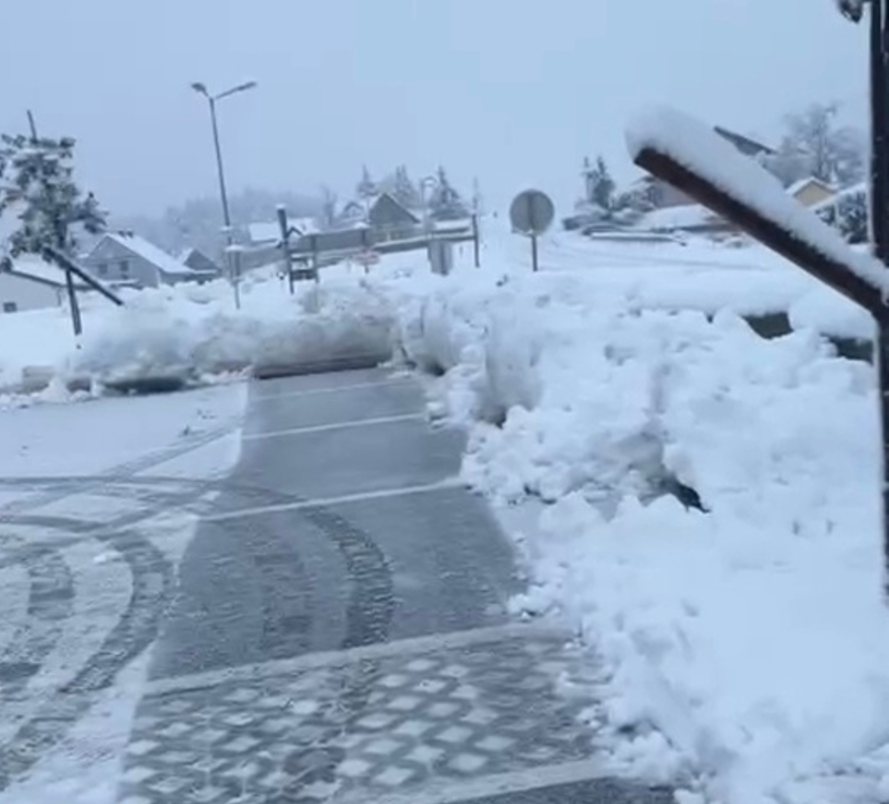 A snowy street with a sidewalk covered in snow, a streetlight, and a signboard. Snow piles are on the sides.
