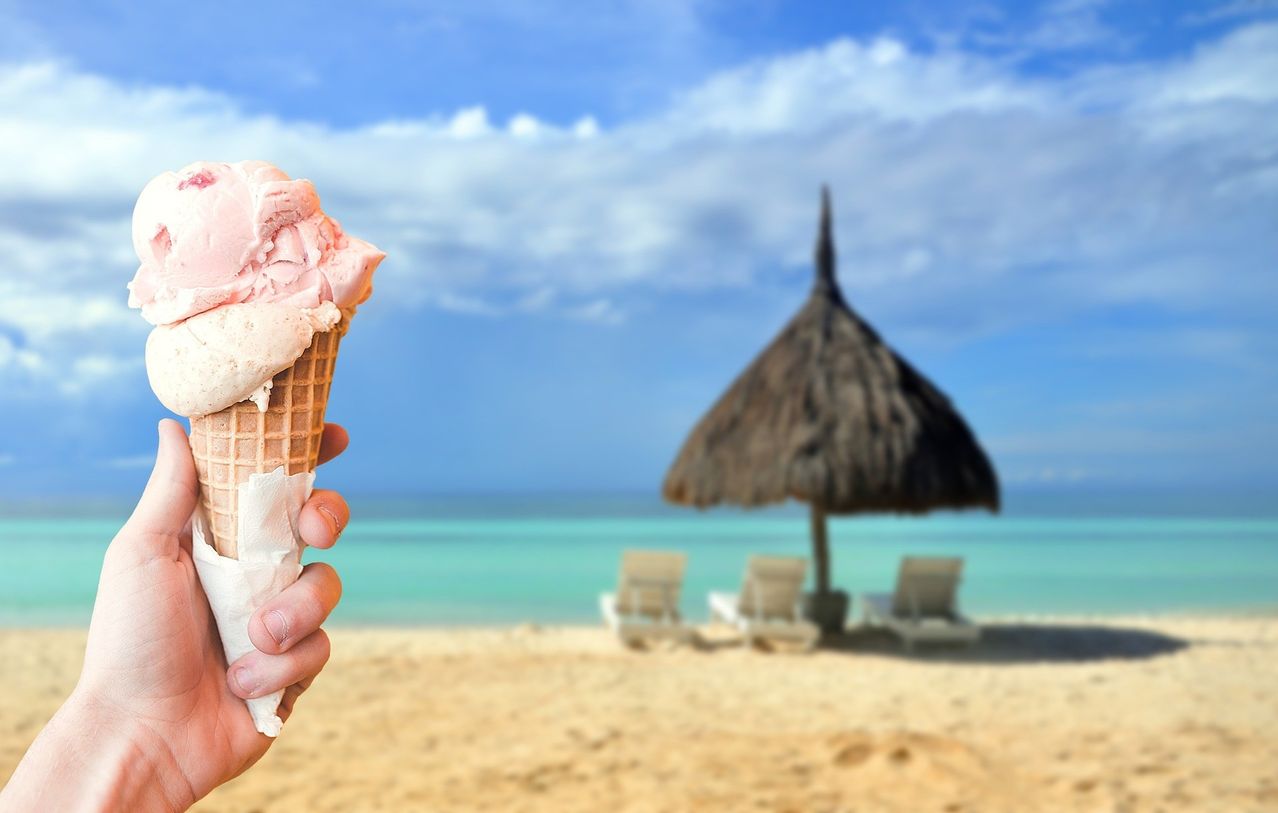 A person holds an ice cream cone on the beach with an umbrella in the background.