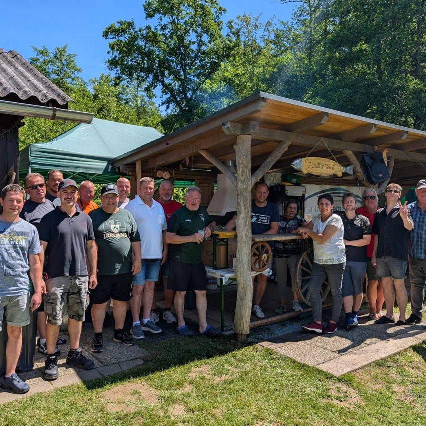 A group of people stands outside a wooden gazebo with a sign reading 'Willy's Tech'. They are dressed casually and smiling for a photo.