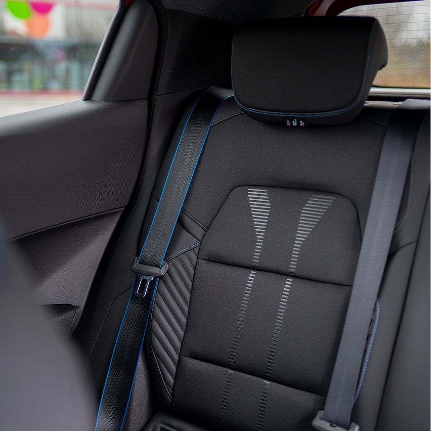 Ein schwarzer Autositz mit blauer Umrandung und einem Sicherheitsgurt, von hinten betrachtet. Der Sitz hat ein strukturiertes Muster.
