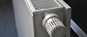 A white radiator with a metal knob for temperature control. The radiator has a ribbed pattern.