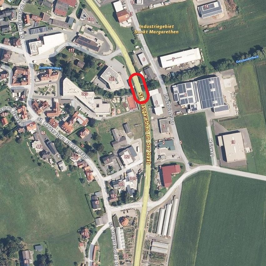 Luftaufnahme einer kleinen Stadt mit Industriegebiet, Wohngebäuden und Straßen. Ein roter Kreis hebt einen bestimmten Bereich auf der St. Margarethen Straße hervor. Gebäude sind mit Nummern und Straßennamen beschriftet.