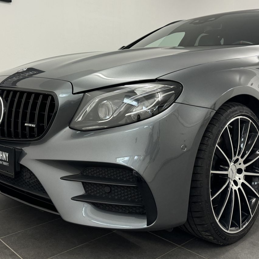Die Vorderseite eines grauen Mercedes-AMG Autos mit schwarzem Kühlergrill und Scheinwerfern. Das Auto steht in einer Ausstellung.