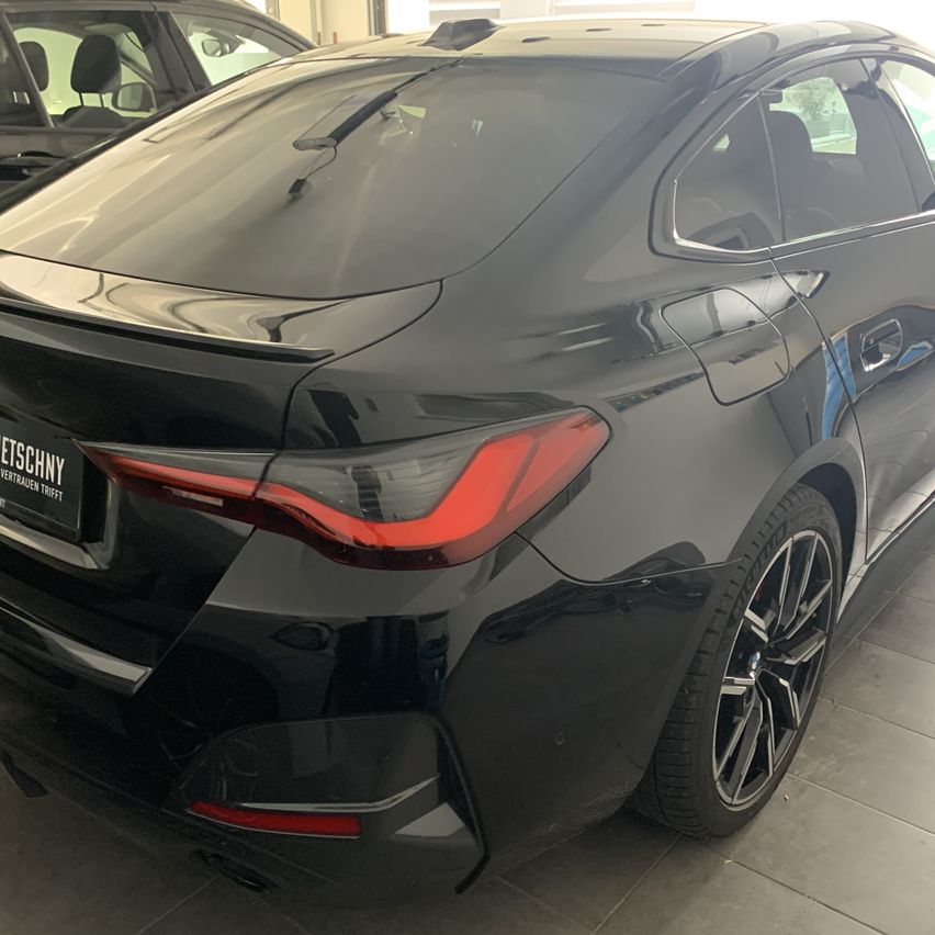 Die Rückseite eines schlanken schwarzen Autos, wahrscheinlich ein Sedan, steht in einer Ausstellung. Es hat rote Rücklichter und Leichtmetallräder.