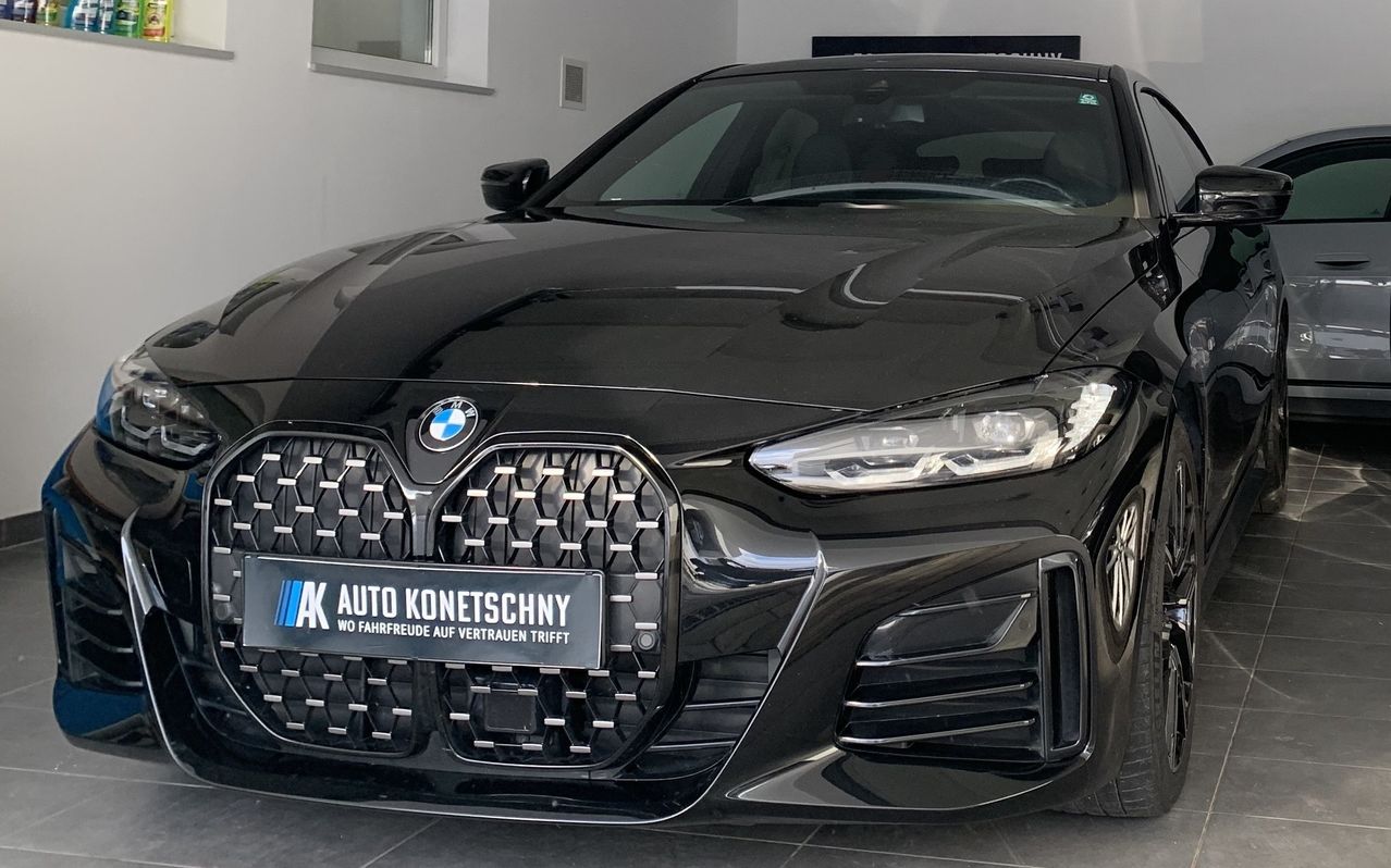 Ein schwarzer BMW-Wagen steht in einem Ausstellungsraum. Er hat ein Nummernschild mit dem Text 'AK AUTO KONETSCHNYY' und einem Slogan. Das Auto hat ein schlankes Design und ein modernes Aussehen.