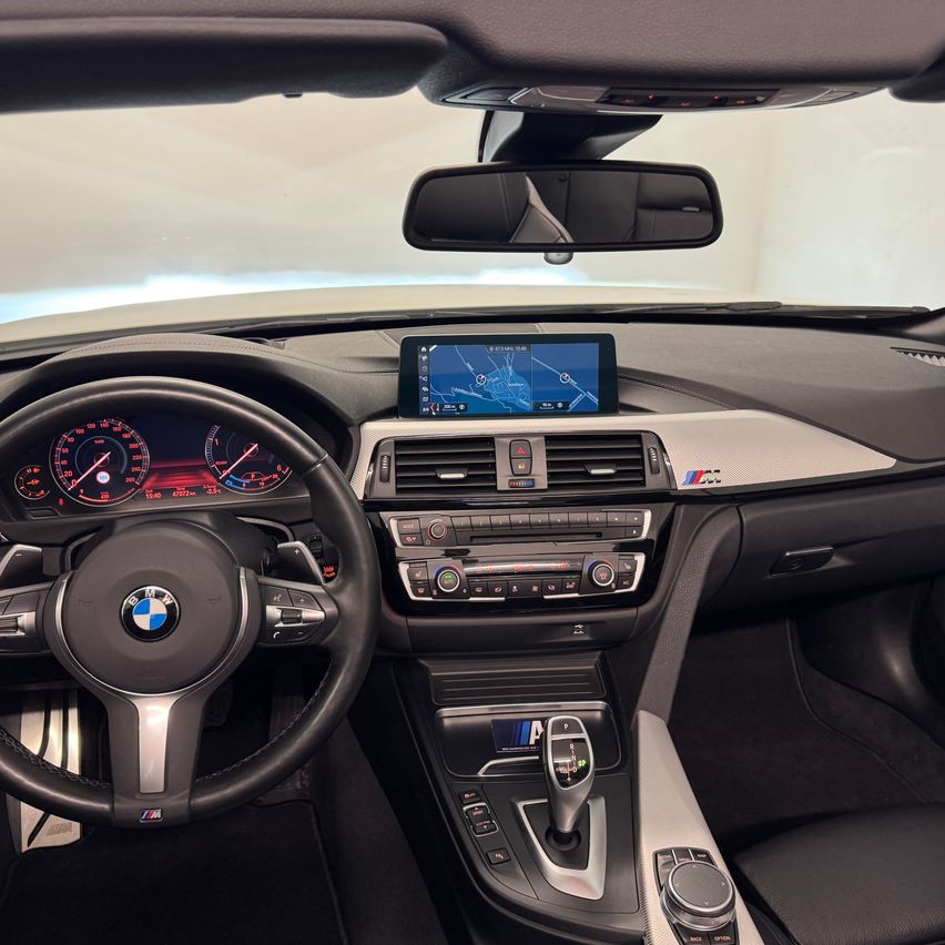 Interior of a BMW car with a dashboard featuring a digital map display, speedometer, and various control buttons. The steering wheel and gear shift are also visible.