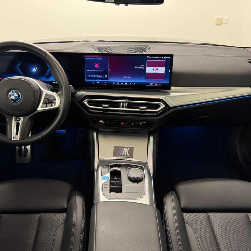 Interior of a BMW car with a digital dashboard showing radio frequency. The dashboard is illuminated with blue light.