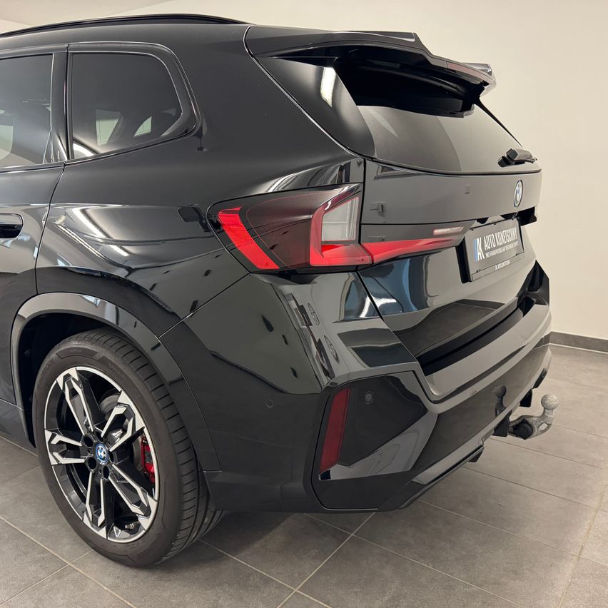The rear end of a black BMW SUV with a spoiler and a license plate is displayed in a showroom.