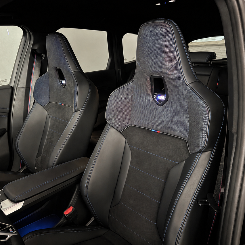 The interior of a luxury car features two black leather seats with blue stitching and a BMW logo on the headrest.
