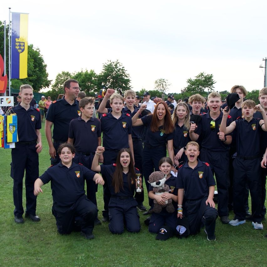 A group of young people in uniforms are posing for a picture, some holding a trophy and a stuffed animal. They are standing on a field.